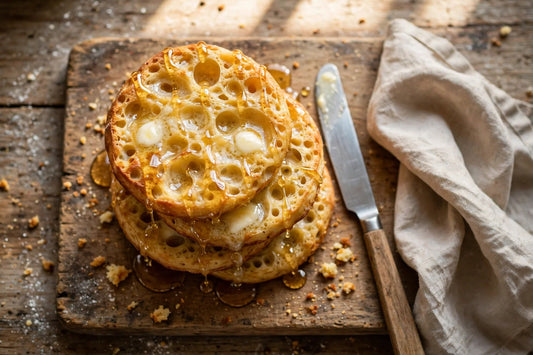 Golden sourdough crumpets with melting butter and honey on a wooden board